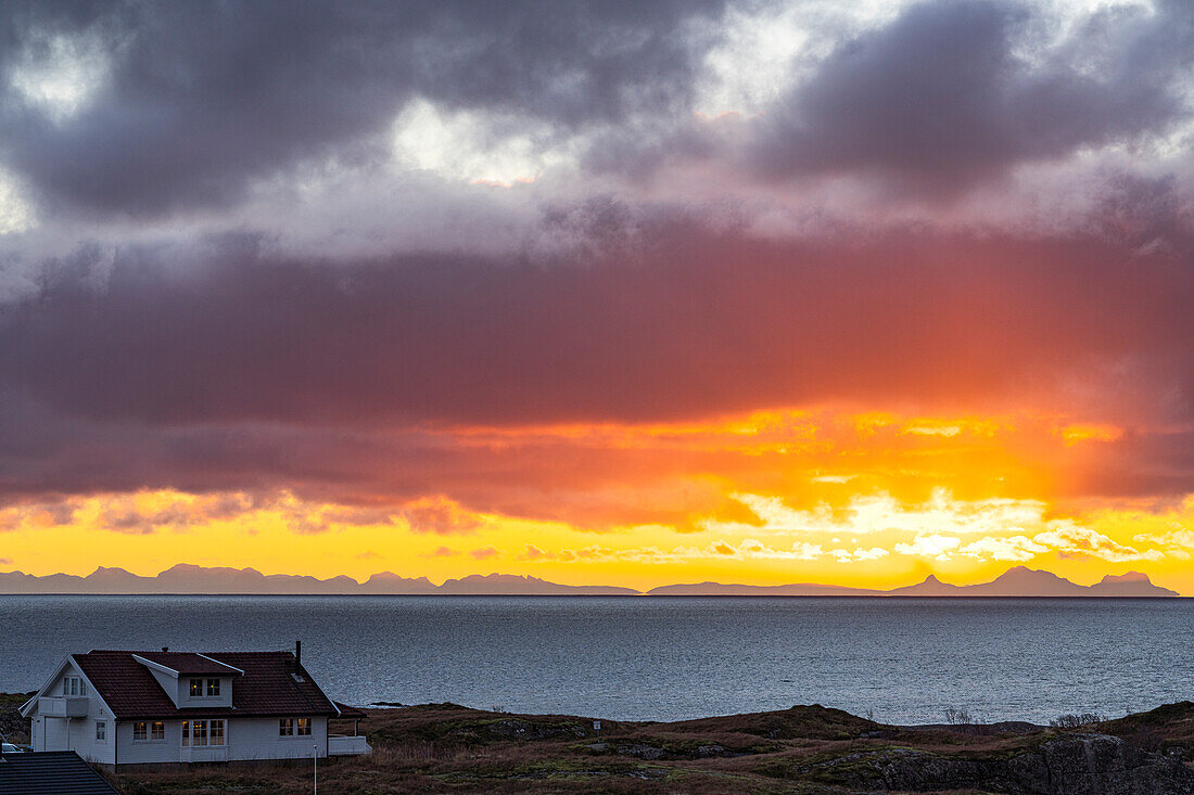 Einsames traditionelles Haus am Meer unter einem dramatischen Himmel in der Morgendämmerung, Reine, Lofoten Inseln, Nordland, Norwegen, Skandinavien, Europa