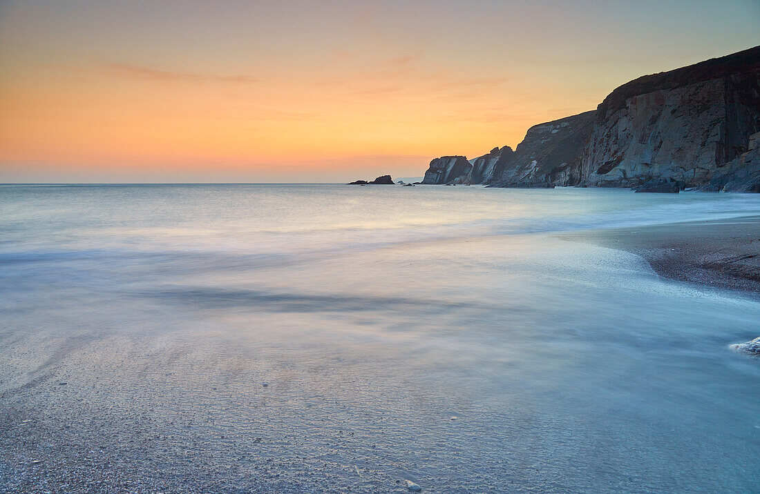 A dusk view of surf surging ashore at Ayrmer Cove, a remote cove near Kingsbridge, south coast of Devon, England, United Kingdom, Europe\n