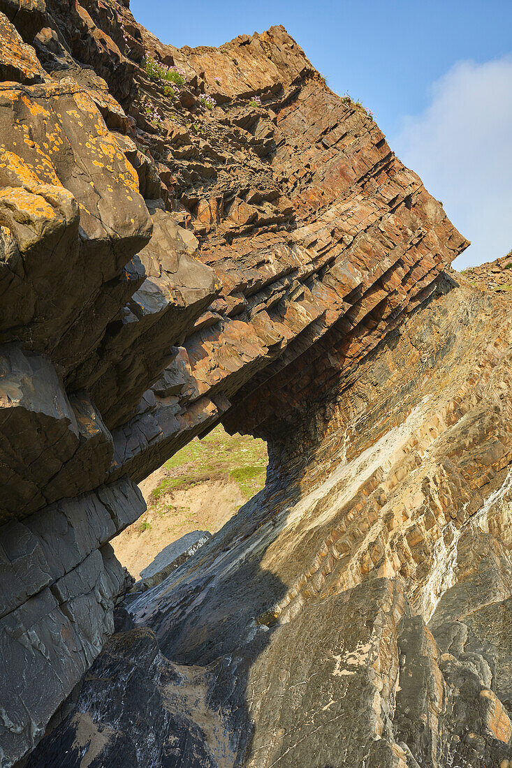A sunlit view of a rock arch, formed from multiple layers of red sedimentary rock, at Hartland Quay, on the Atlantic coast of Devon, England, United Kingdom, Europe\n