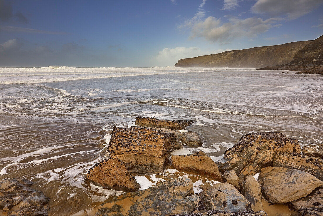 Der Sand, die Felsen, die Brandung, die Klippen und die Gewitterwolken an Cornwalls Atlantikküste, am Trebarwith Strand, nahe Tintagel, Cornwall, England, Vereinigtes Königreich, Europa