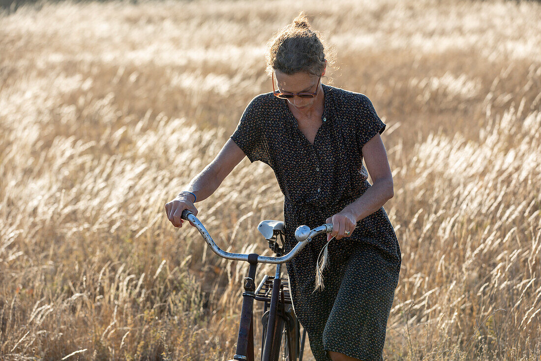 Frau schiebt Fahrrad im Sommer, Weizenfeld im Hintergrund