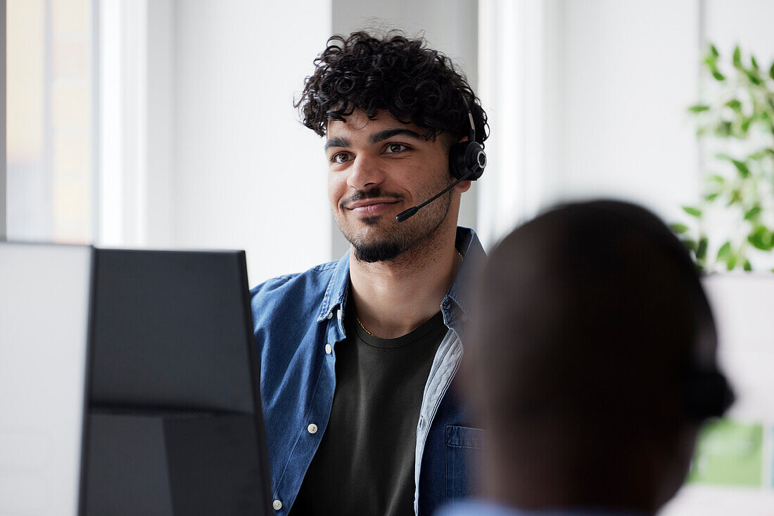 Junger Mann benutzt ein Headset, während er im Büro sitzt