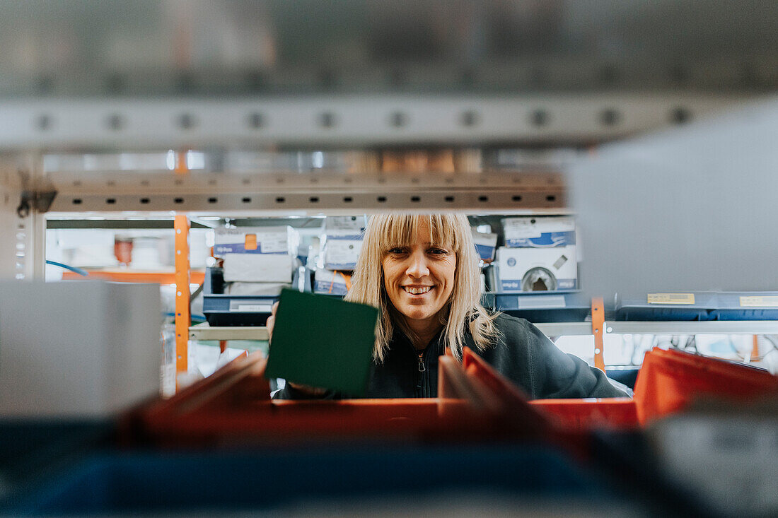Portrait of smiling female worker taking equipment from shelf\n