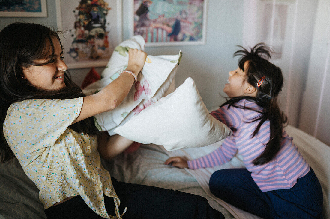 Happy sisters having pillow fight at home\n