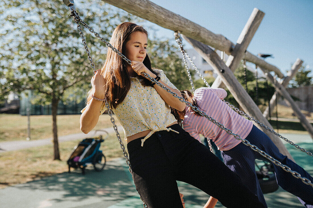 Sisters having fun swinging on swing on playground\n