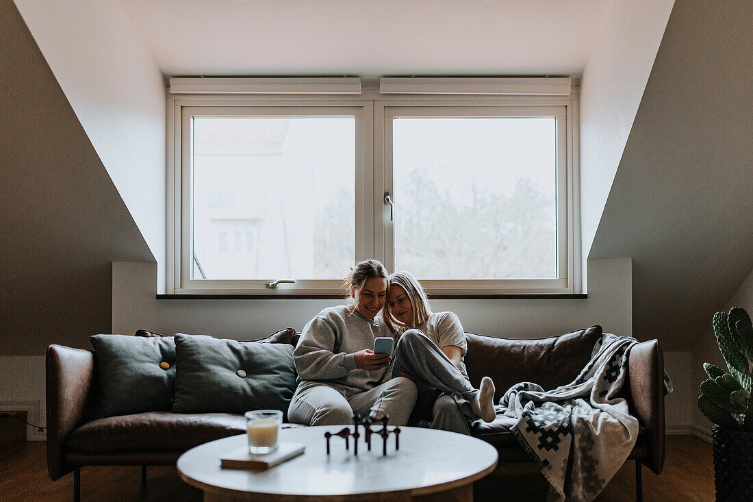 Female couple sitting together on sofa and looking at cell phone\n