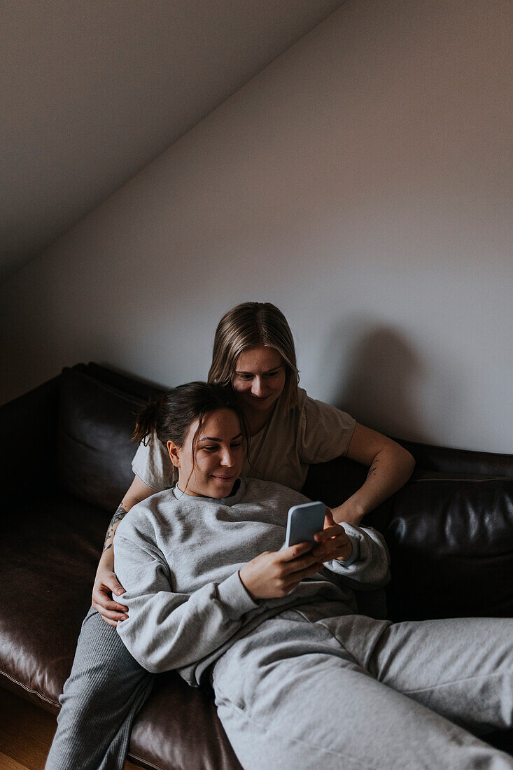 Female couple relaxing together on sofa and looking at cell phone\n
