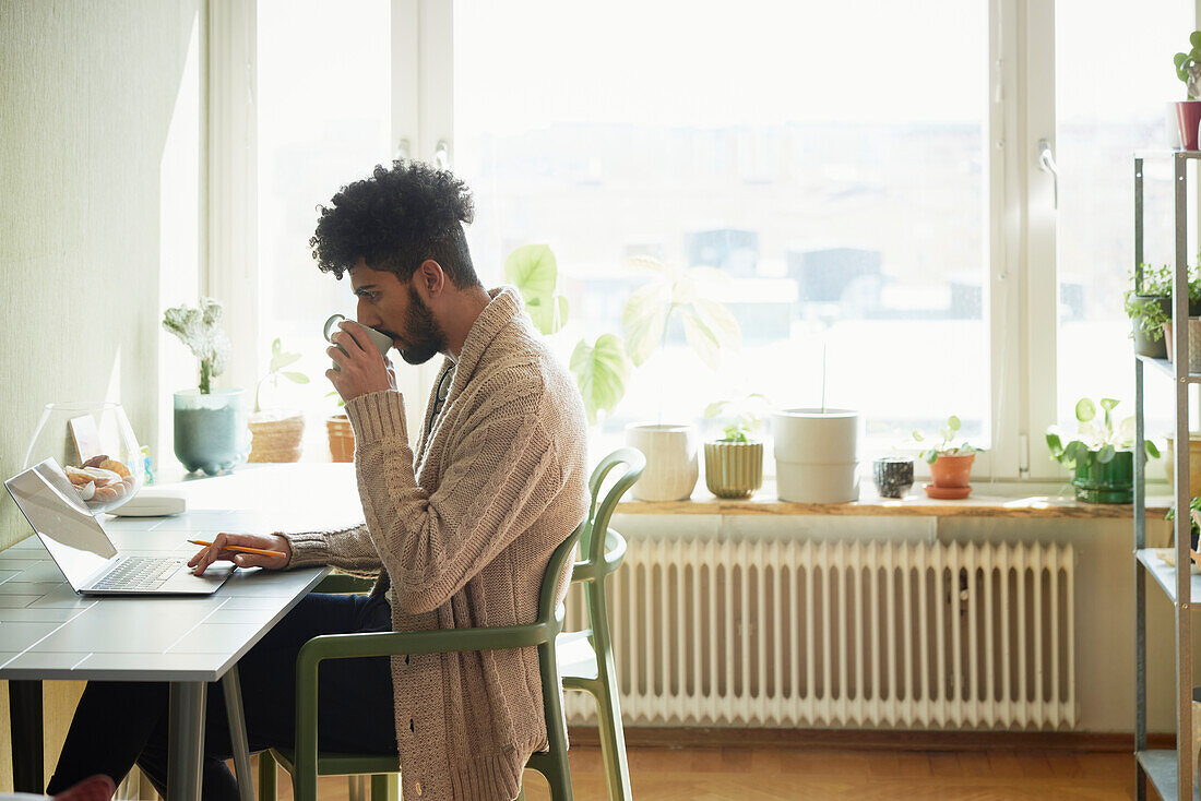 Man using laptop at table while drinking coffee\n