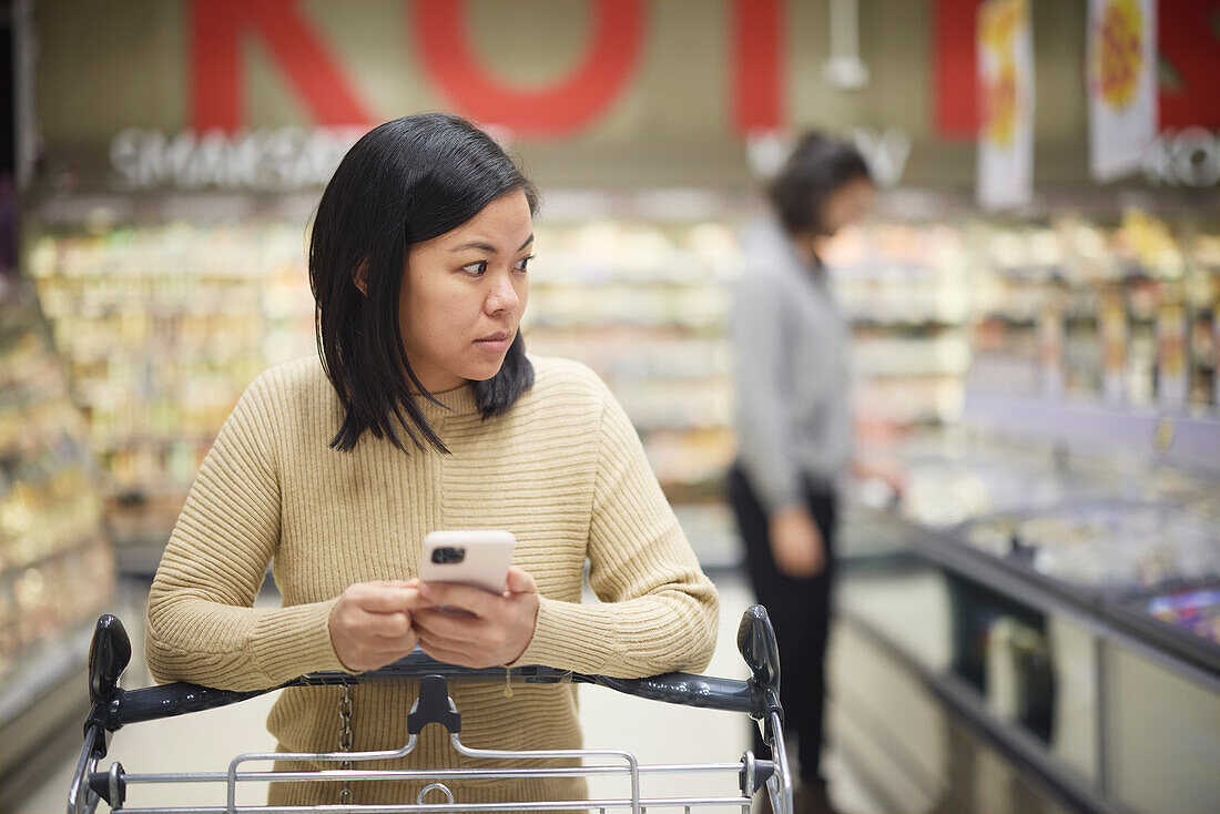 Woman doing shopping in supermarket and holding cell phone\n