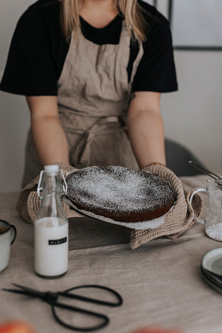 Woman putting freshly baked chocolate cake on table\n