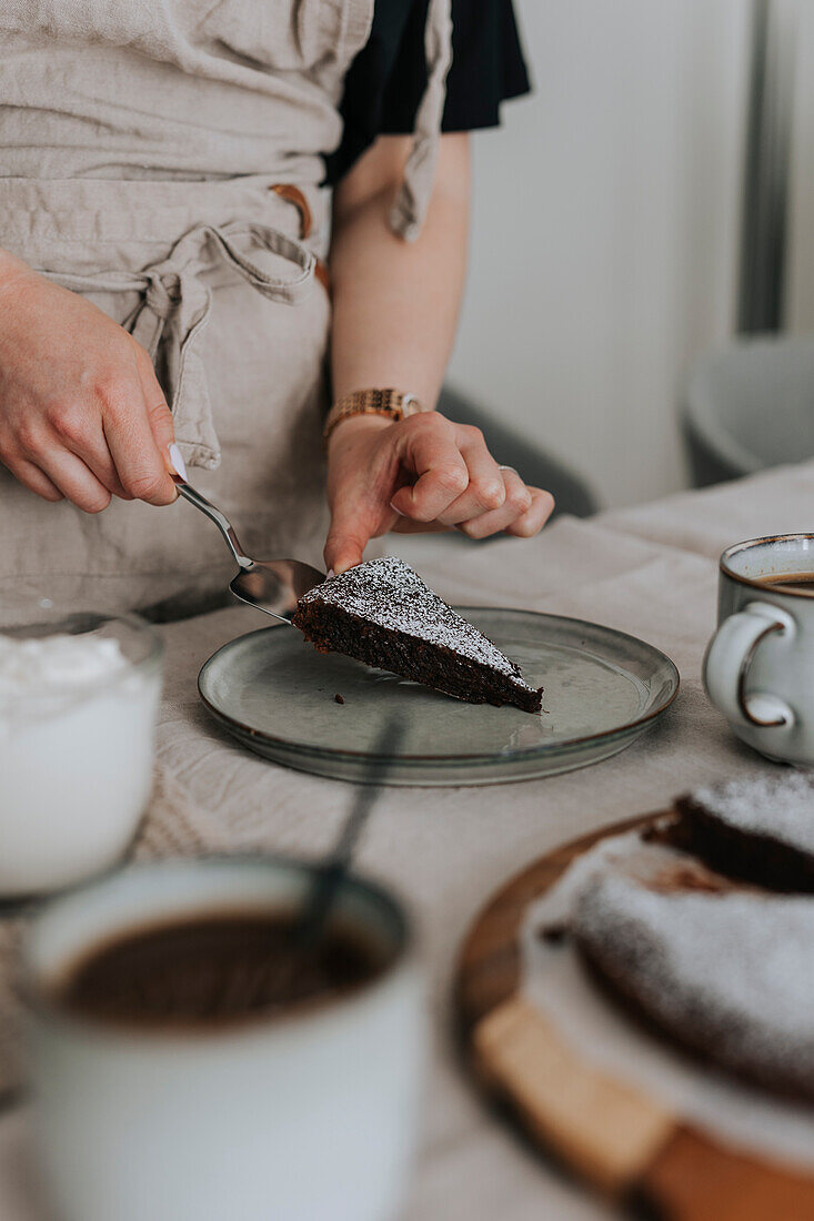 Woman putting piece of freshly baked chocolate cake on plate\n