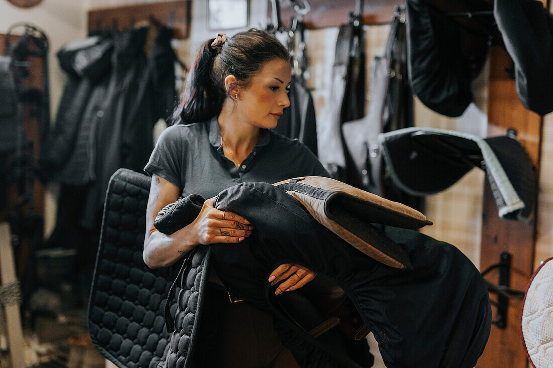 Woman in stable carry saddle and looking away\n