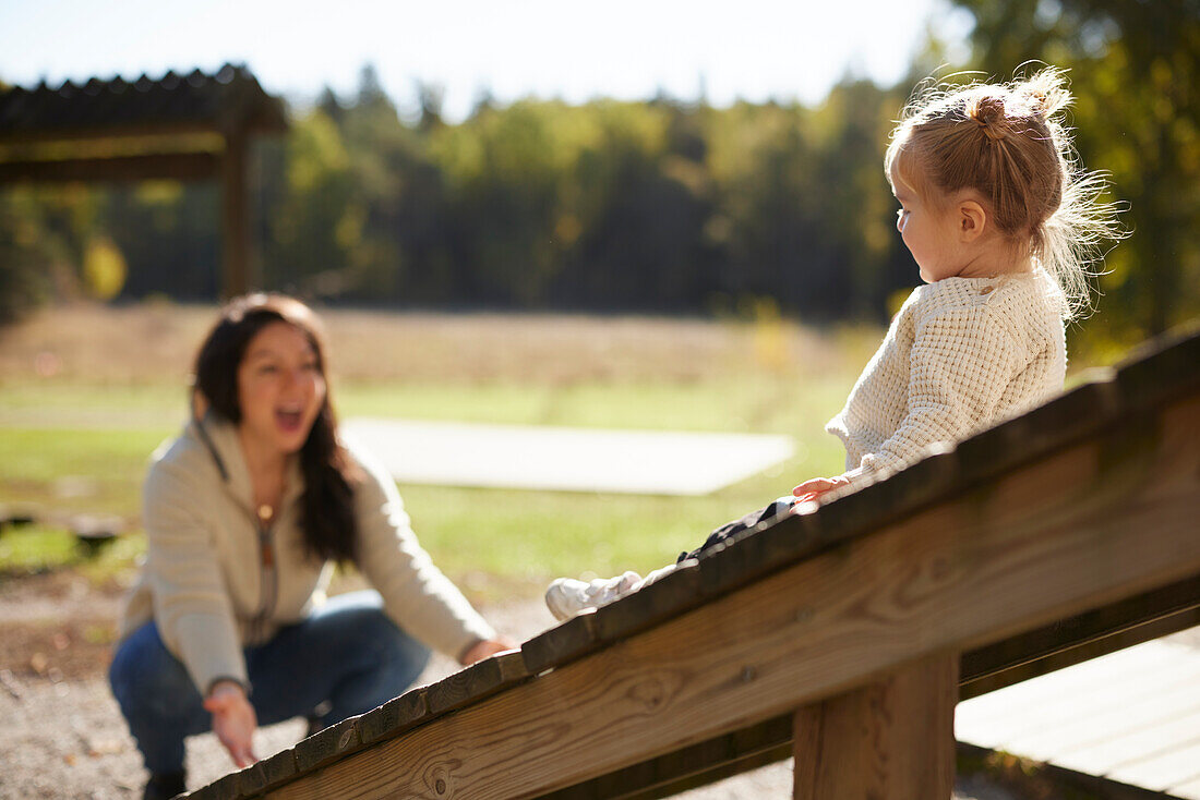 Mutter schaut Tochter beim Spielen auf dem Spielplatz zu