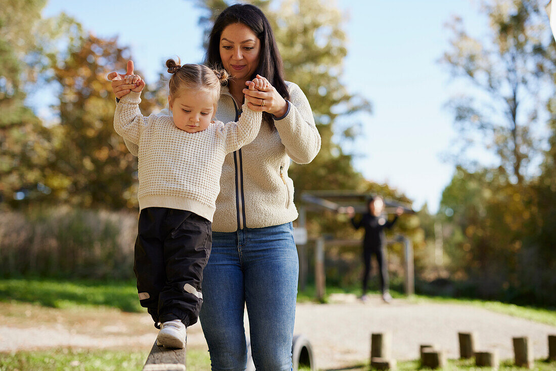 Mother helping daughter to keep balance at playground\n