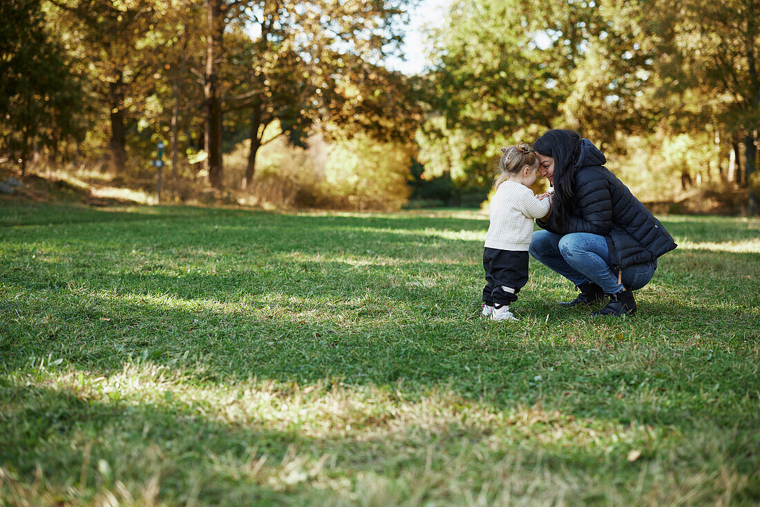 Mother and daughter standing together in autumn park\n