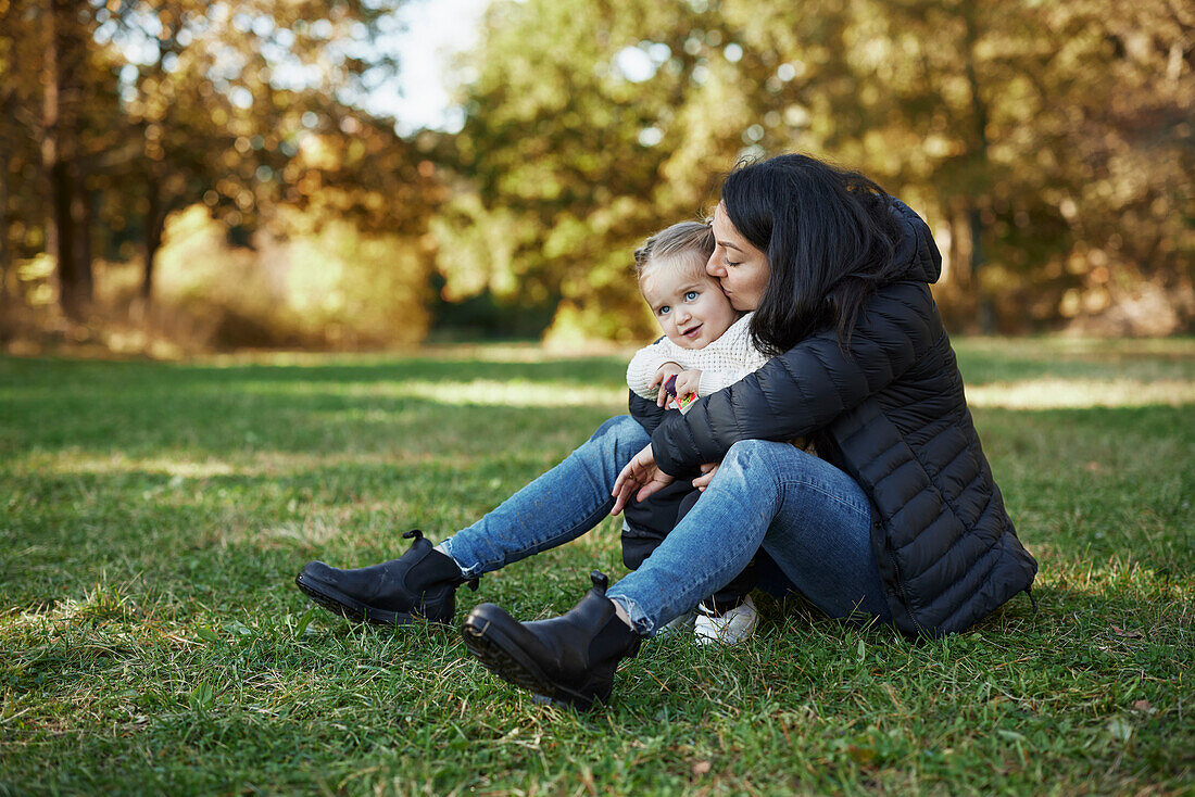 Mother and daughter sitting and hugging in autumn park\n