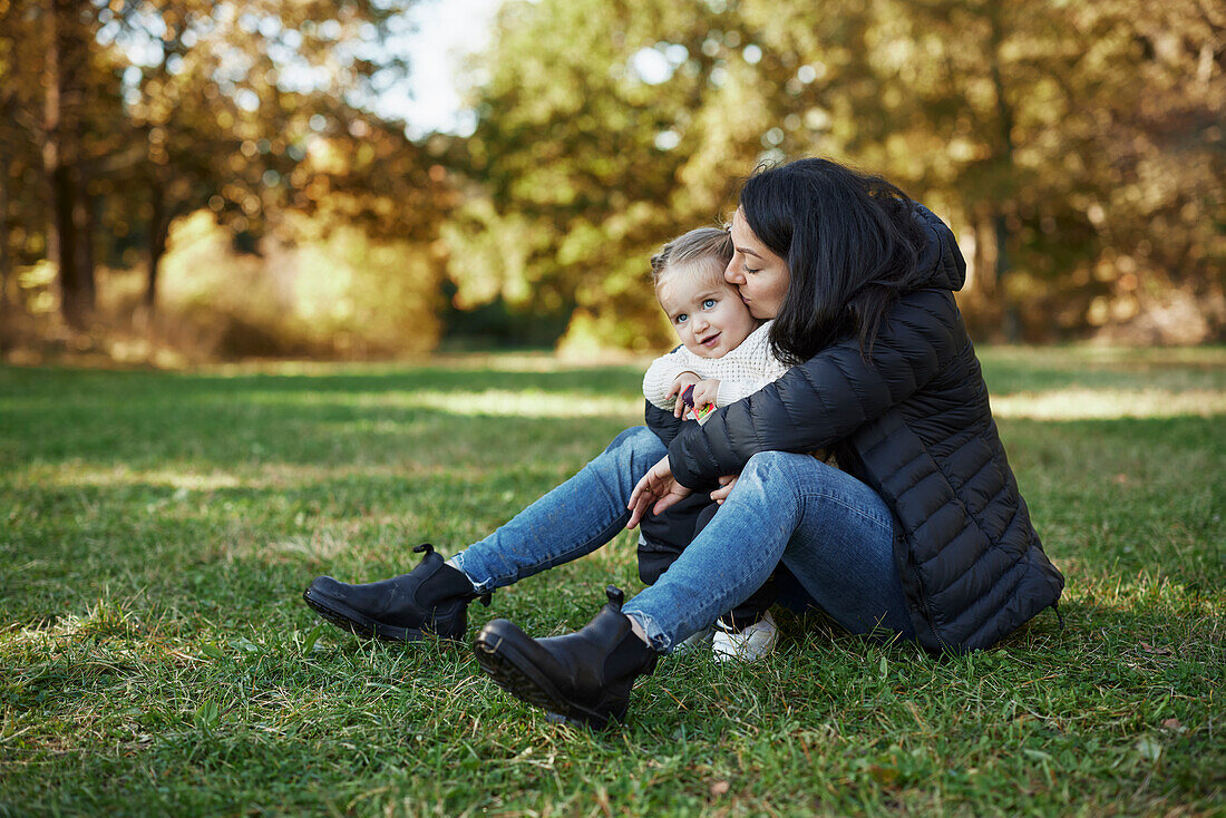Mutter und Tochter sitzen und umarmen sich im Herbstpark