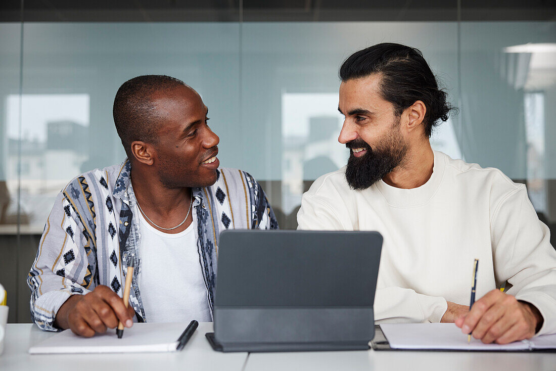 Smiling coworkers sitting at business meeting and looking at each other\n