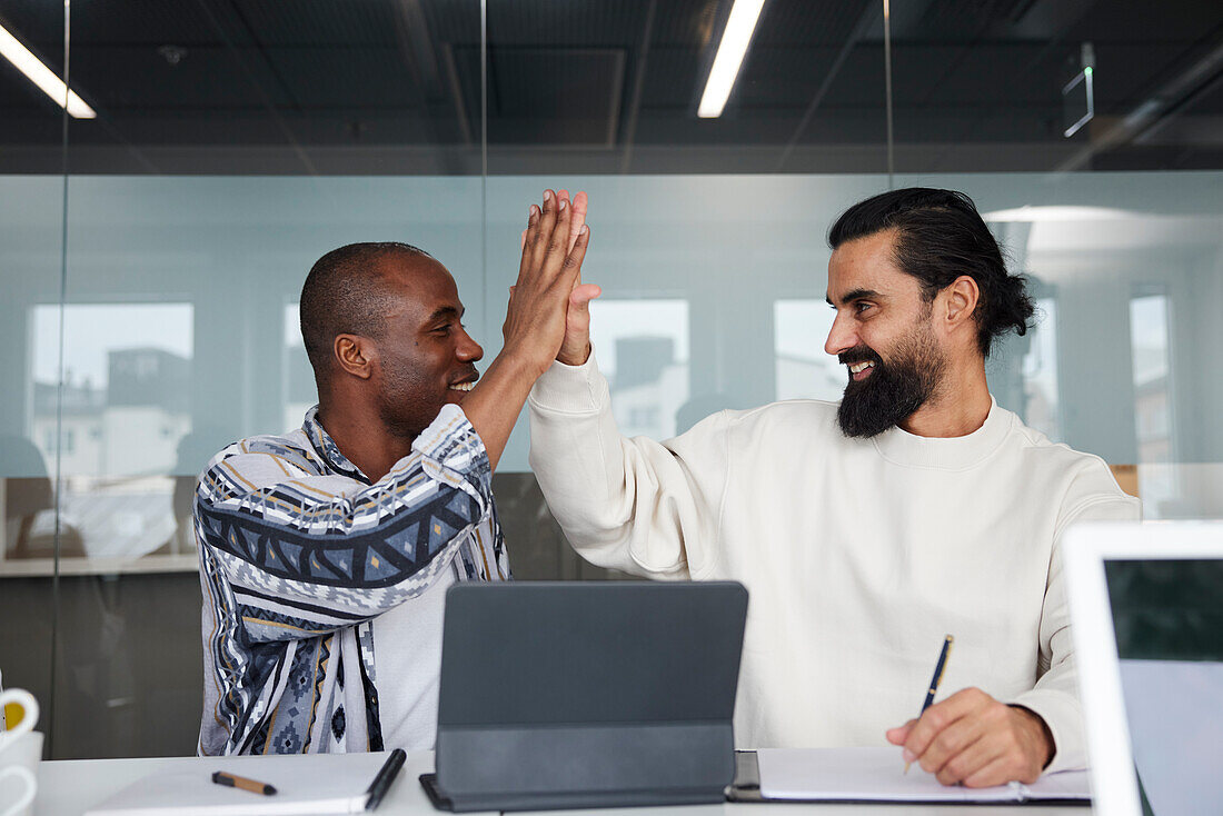 Smiling coworkers sitting at business meeting and giving each other high five\n