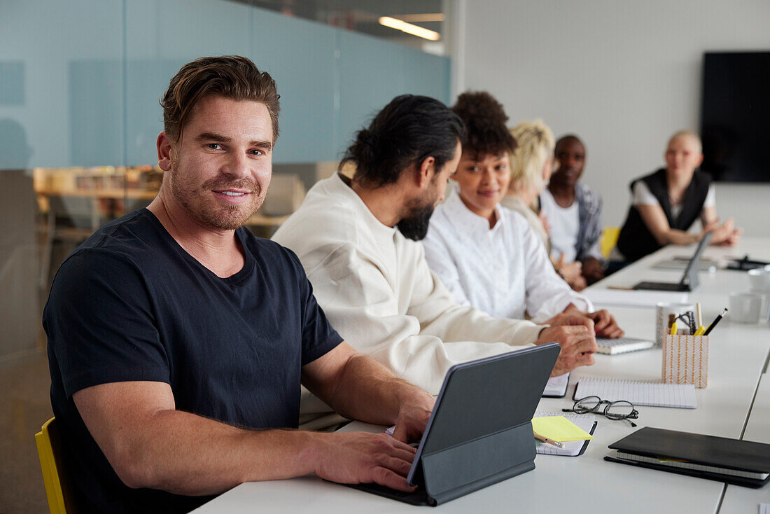 Man sitting at business meeting with digital tablet and looking at camera\n