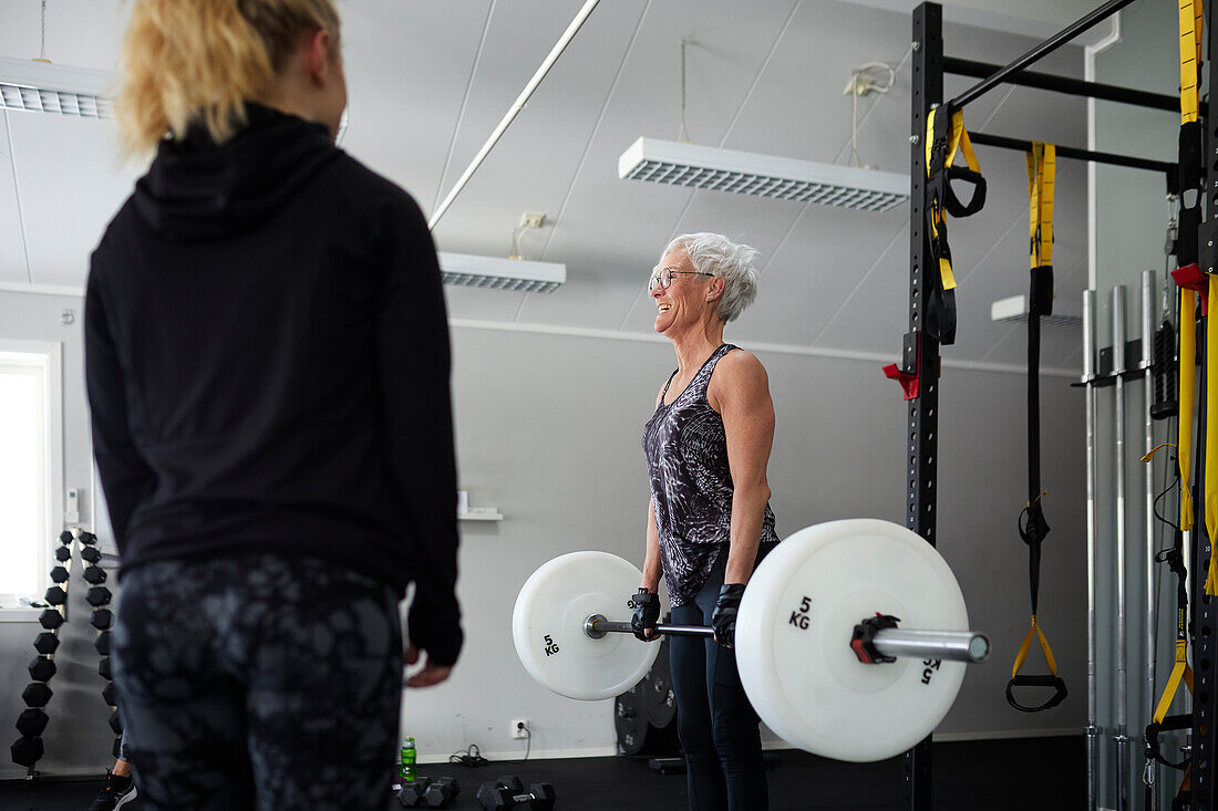 Mid adult woman looking at senior woman lifting weights\n