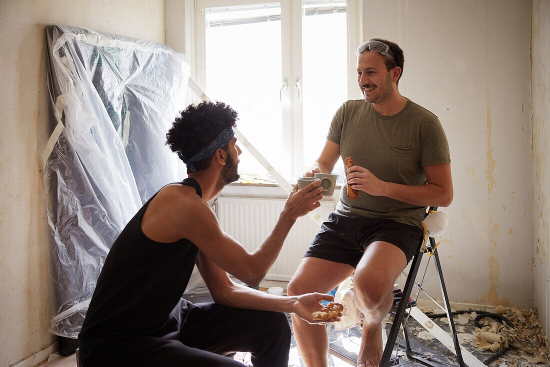 Lächelndes männliches homosexuelles Paar bei der Kaffeepause während der Wohnungsrenovierung