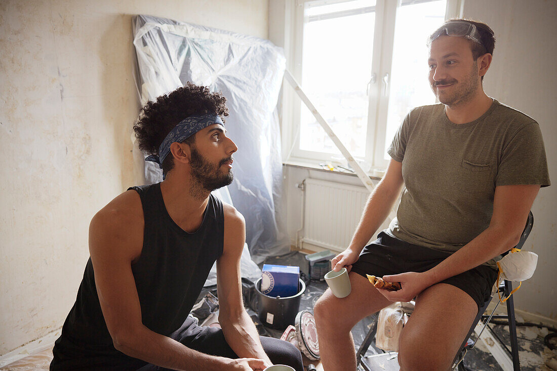 Smiling male homosexual couple having coffee break during apartment renovation\n