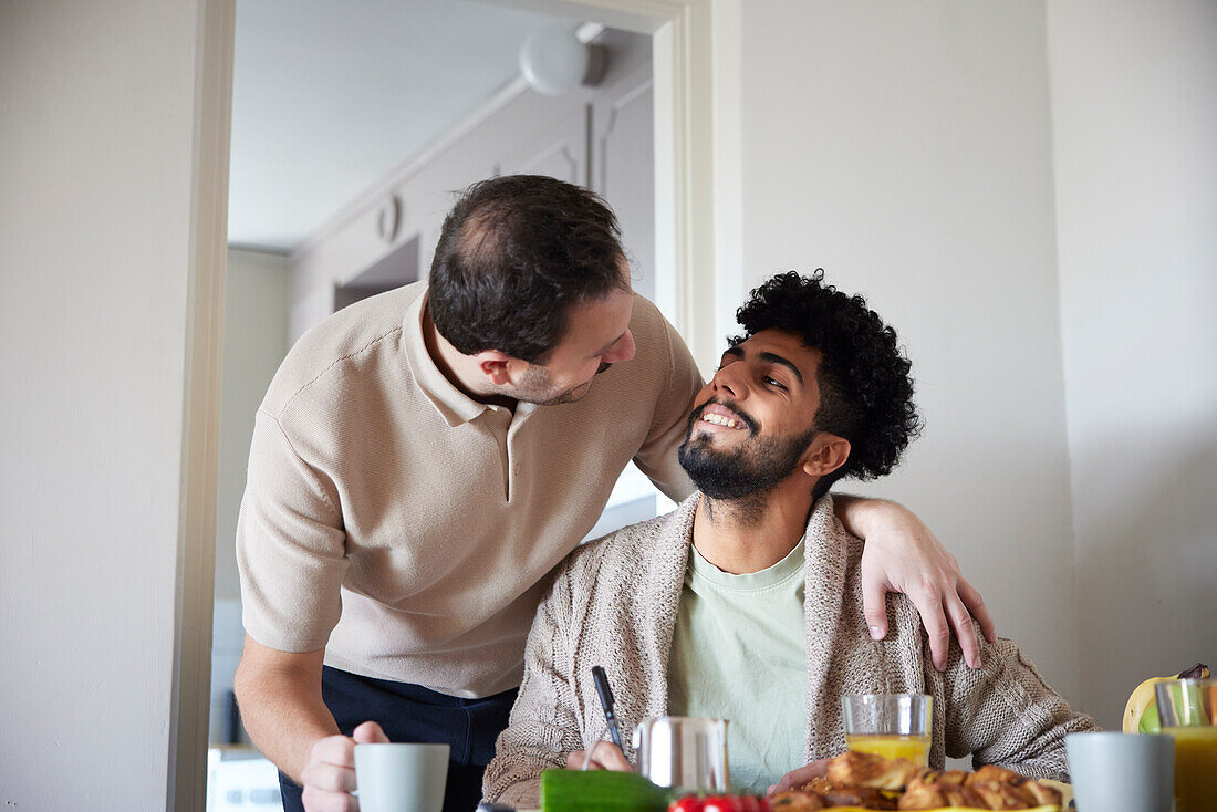 Happy gay couple eating breakfast at home\n