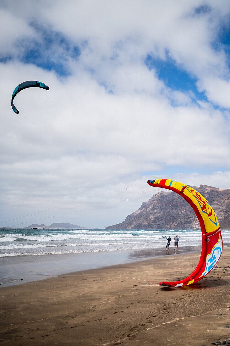 Kite-Surfer am Strand von Famara (Playa de Famara), einem 6 km langen goldenen Sandstrand im Naturpark des Chinijo-Archipels, zwischen dem Fischerdorf La Caleta de Famara und dem Fuß der beeindruckenden Klippen von Famara, Lanzarote, Kanarische Inseln, Spanien