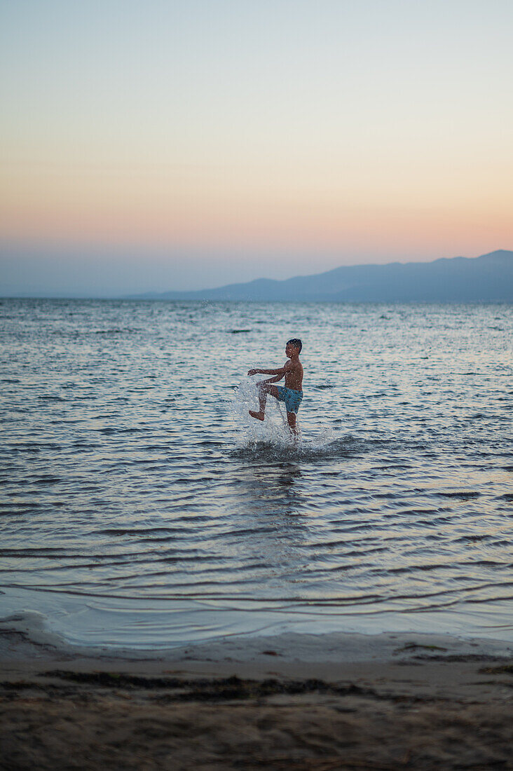 Junger Junge spielt bei Sonnenuntergang am Strand von Trabucador, Ebro-Delta, Tarragona, Spanien