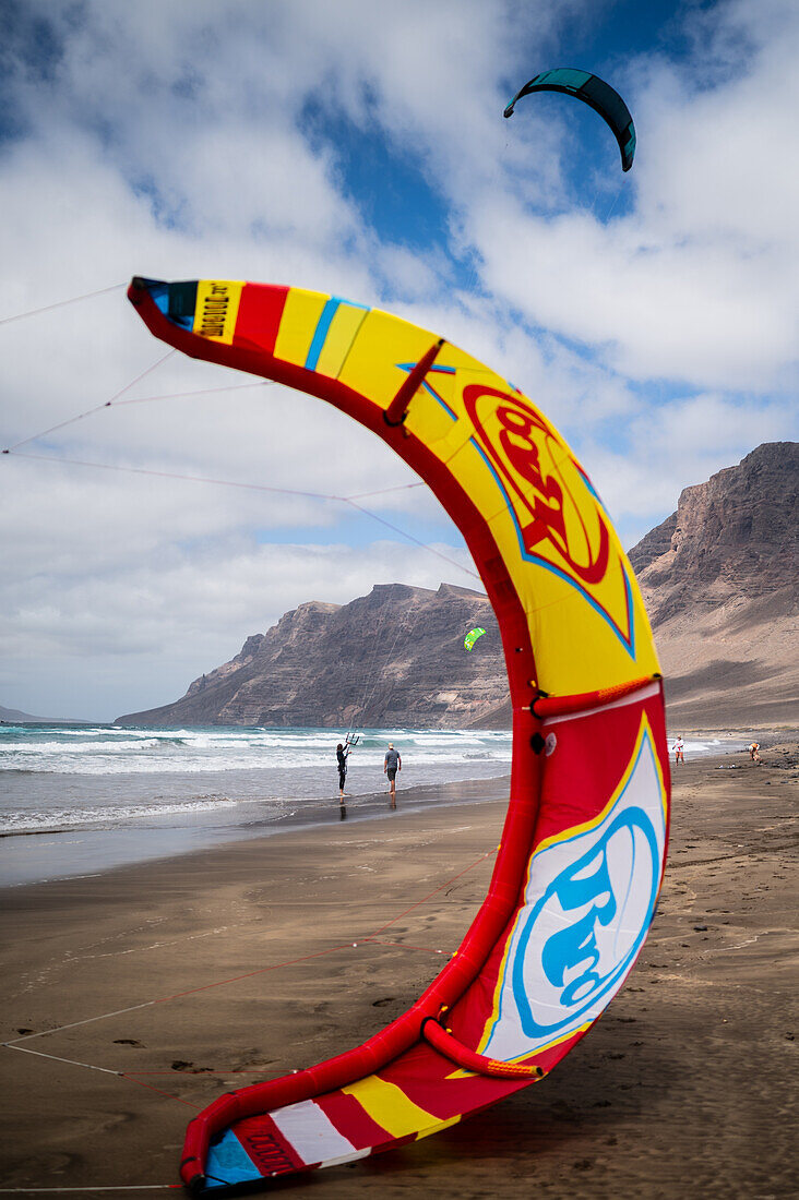 Kite-Surfer am Strand von Famara (Playa de Famara), einem 6 km langen goldenen Sandstrand im Naturpark des Chinijo-Archipels, zwischen dem Fischerdorf La Caleta de Famara und dem Fuß der beeindruckenden Klippen von Famara, Lanzarote, Kanarische Inseln, Spanien