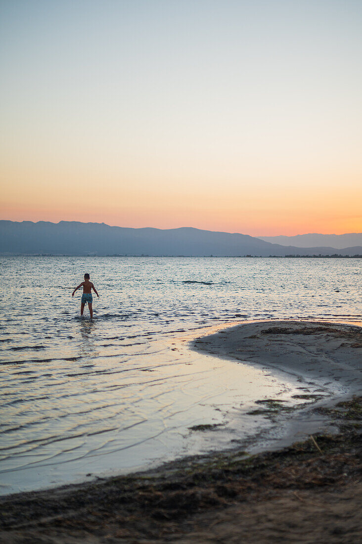 Junger Junge spielt bei Sonnenuntergang am Strand von Trabucador, Ebro-Delta, Tarragona, Spanien