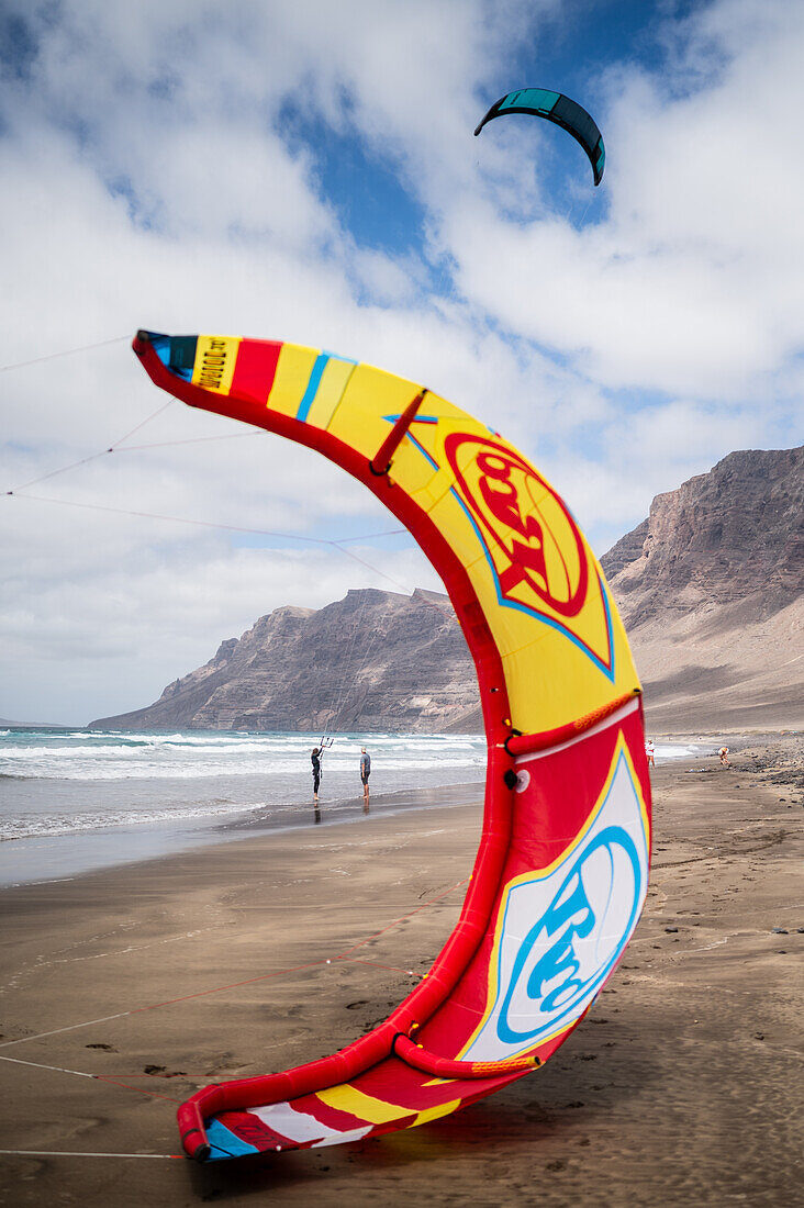 Kite-Surfer am Strand von Famara (Playa de Famara), einem 6 km langen goldenen Sandstrand im Naturpark des Chinijo-Archipels zwischen dem Fischerdorf La Caleta de Famara und dem Fuß der beeindruckenden Klippen von Famara, Lanzarote, Kanarische Inseln, Spanien