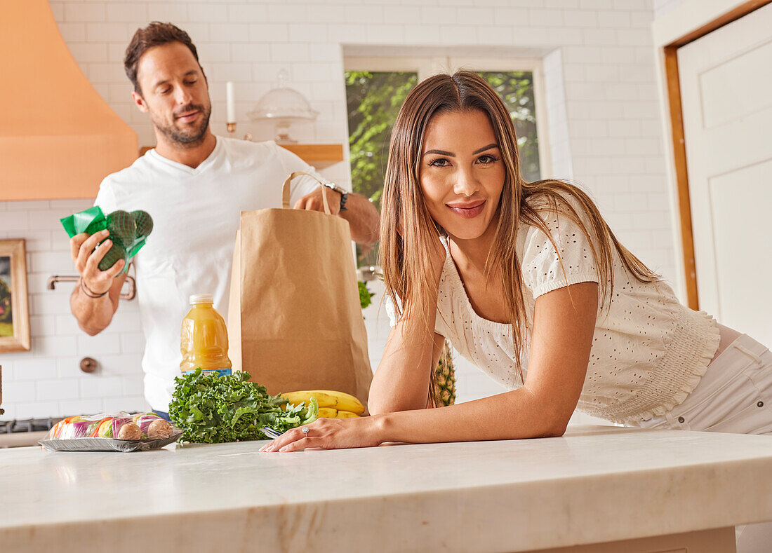 Lächelndes Paar mit Papiertüte und Lebensmitteln in der Küche