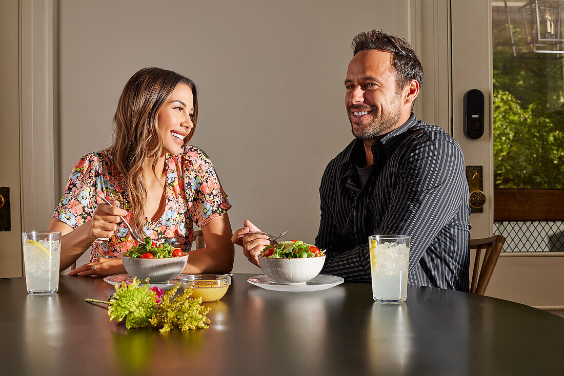 Smiling couple enjoying salad at table at home\n