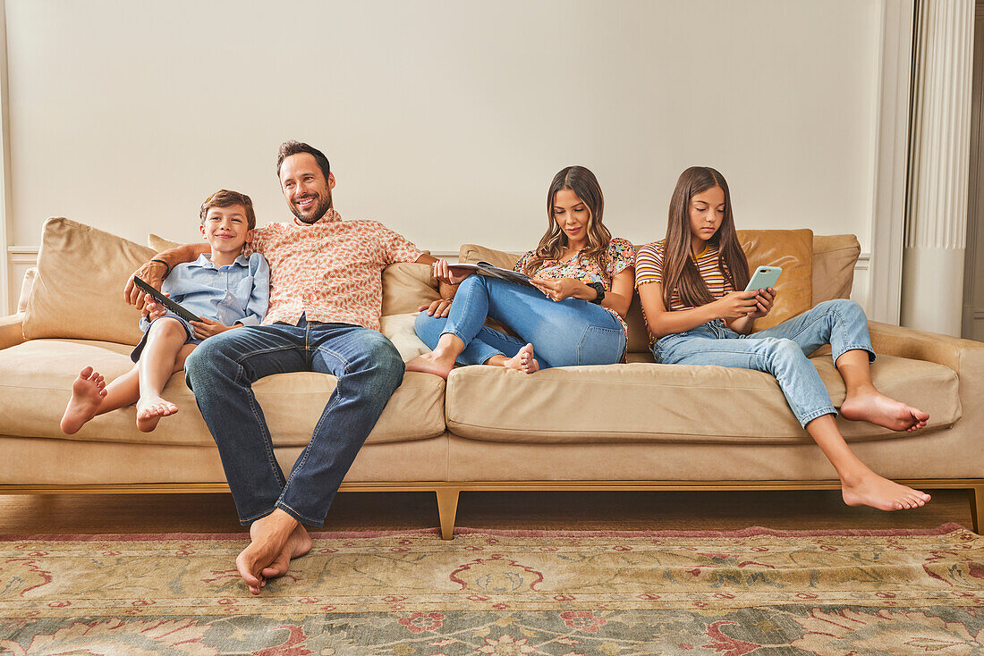 Smiling family with two children (8-9, 12-13) relaxing on sofa\n
