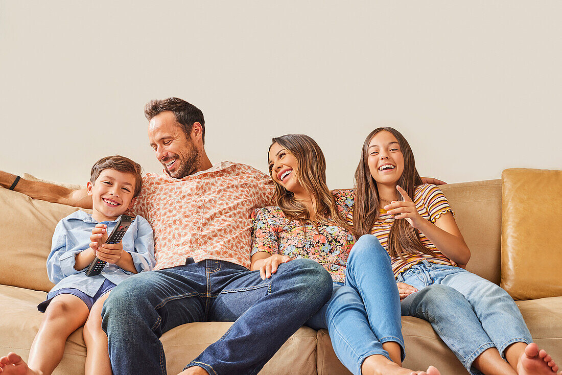 Smiling family with two children (8-9, 12-13) watching TV on sofa\n