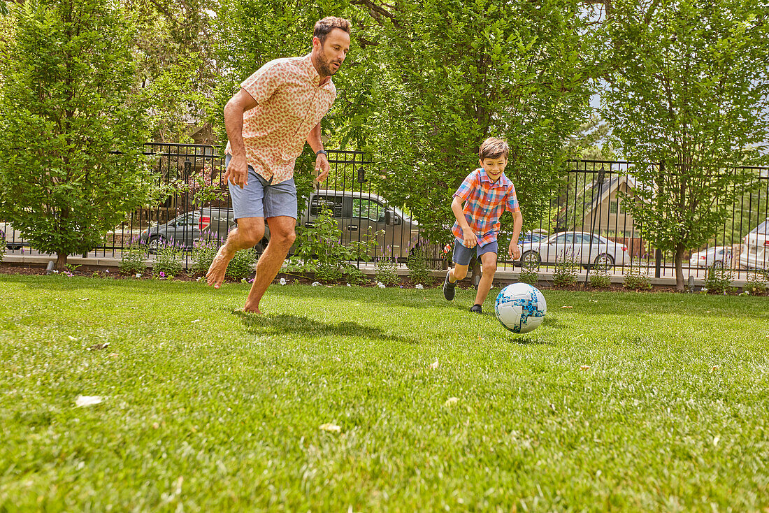 Father and son (8-9) playing soccer in park\n