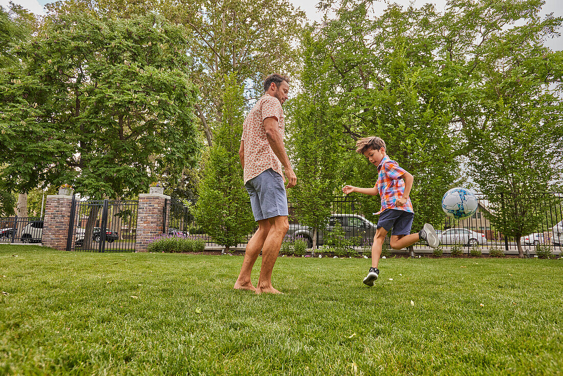 Father and son (8-9) playing soccer in park\n