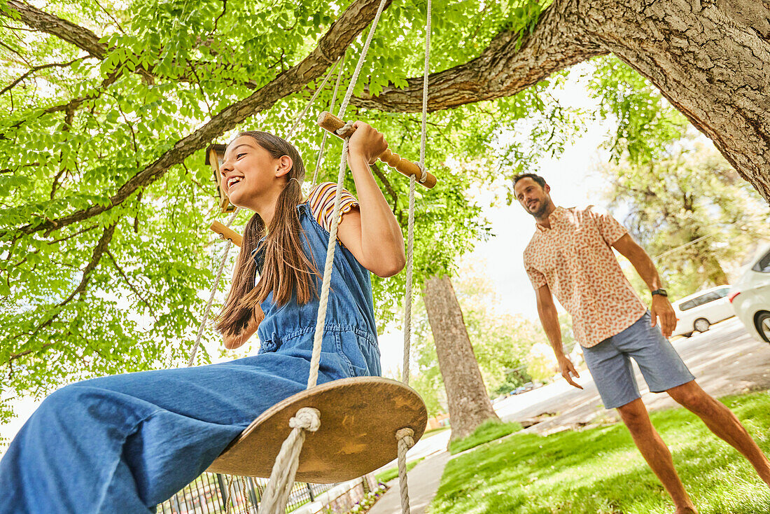 Smiling girl (12-13) on swing in park, father in background\n