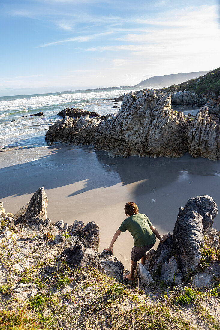 Südafrika, Hermanus, Junge (10-11) erkundet felsige Küste in Voelklip Beach