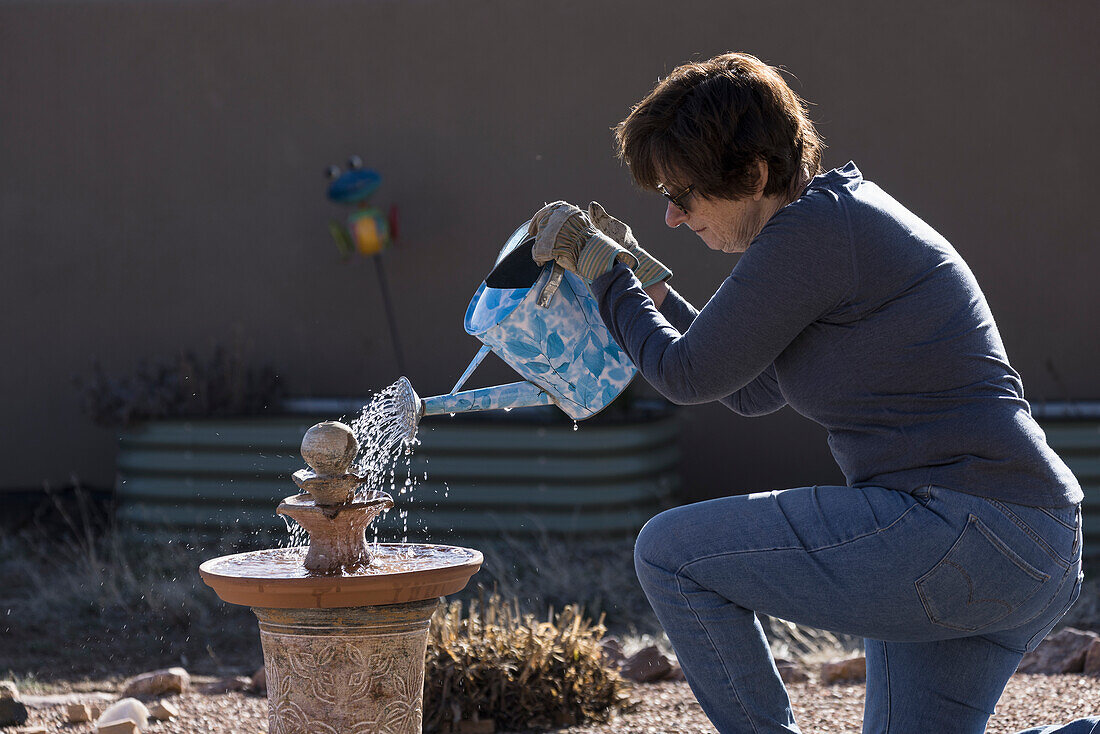 Woman filling bird bath with watering can\n