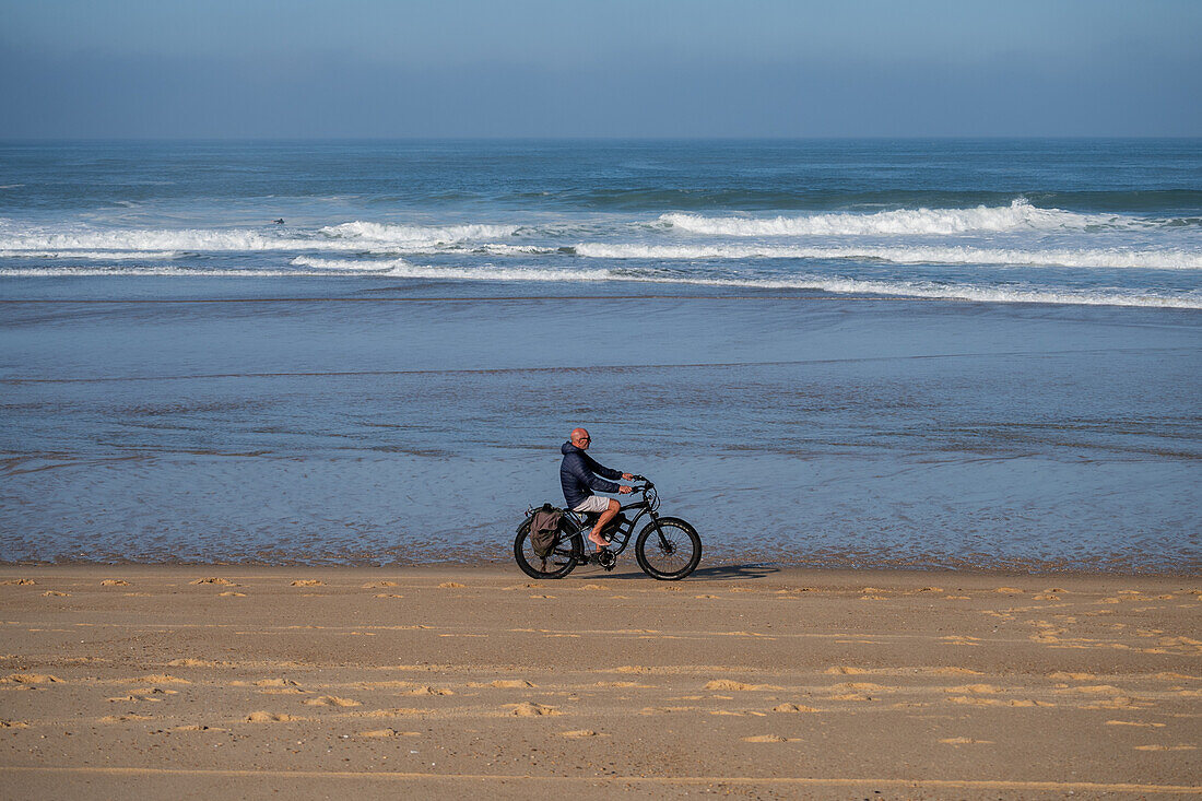 Ein Mann fährt mit seinem Elektrofahrrad am Strand von Les Culs Nus, Hossegor, Landes, Frankreich.
