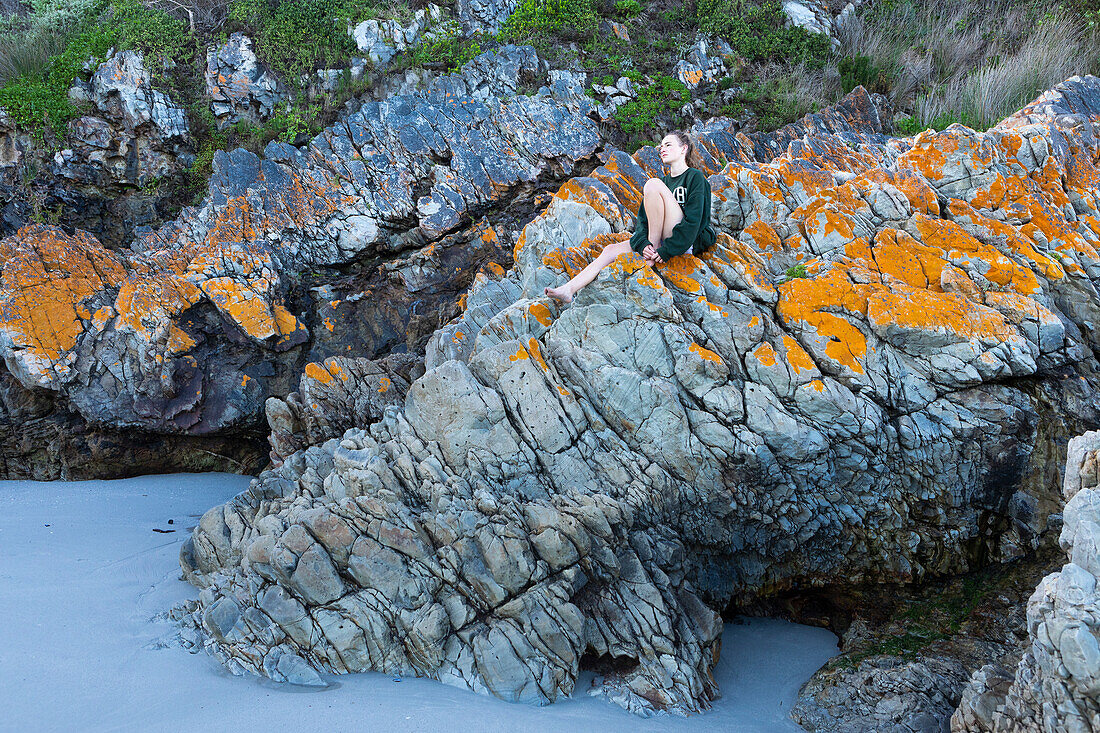 Thoughtful teenage girl (16-17) sitting on rock in Voelklip Beach\n