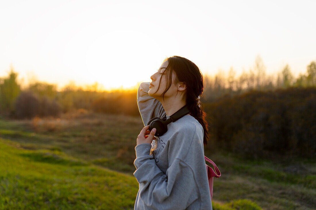 Portrait of young woman with headphones on meadow at sunset\n