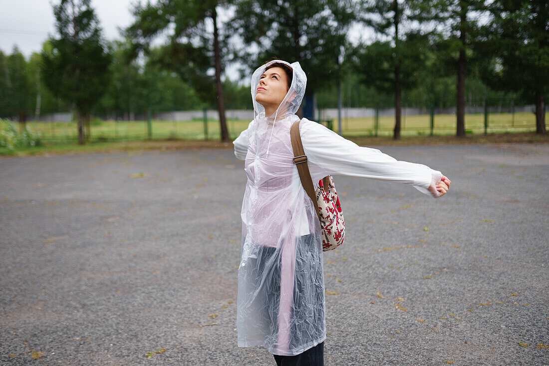 Portrait einer jungen Frau mit ausgestreckten Armen im Regen
