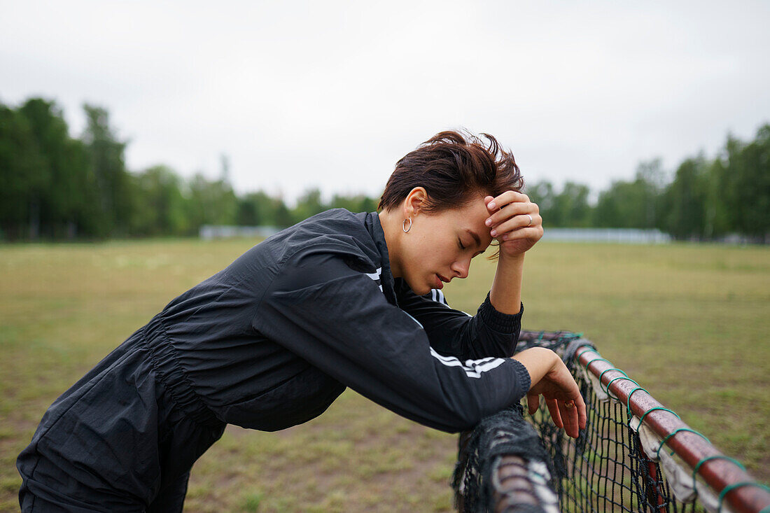 Side view of young woman leaning on mini soccer goal\n