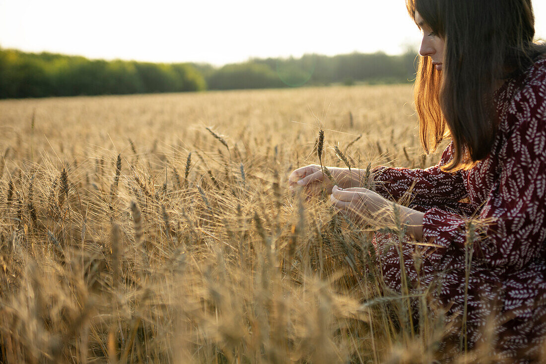 Side view of woman touching cereal plant in field\n