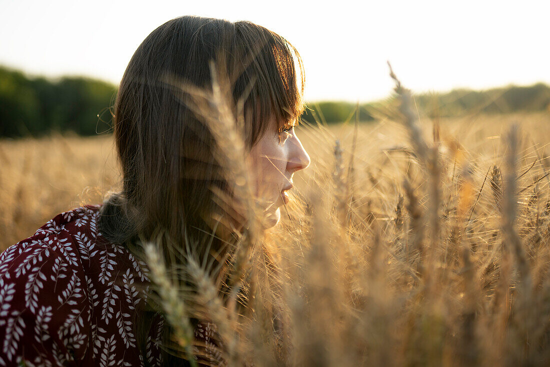 Portrait einer jungen Frau mit Blick auf ein landwirtschaftliches Feld bei Sonnenuntergang