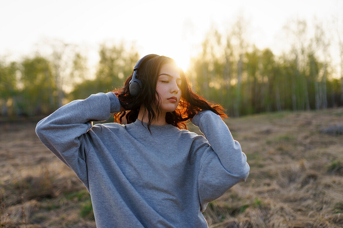 Portrait einer Frau, die mit geschlossenen Augen auf einer Wiese bei Sonnenuntergang Musik hört